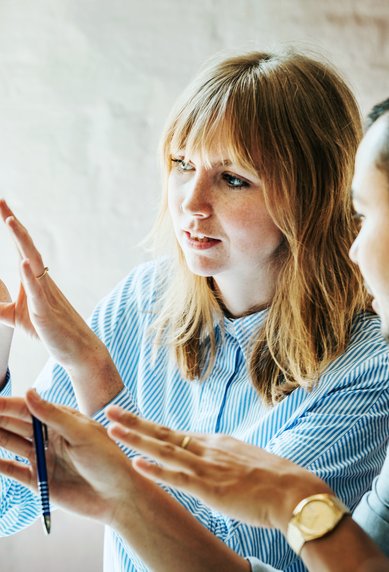 Qualitätsbeauftragte diskutieren an einem Computer, während die Frau mit ihren Händen gestikuliert. Beide scheinen an einem Projekt oder einer Präsentation zu arbeiten.